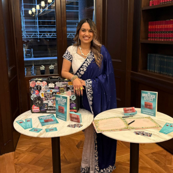Woman in blue saree smiling beside tables displaying “The Briefcase Effect” books and materials.